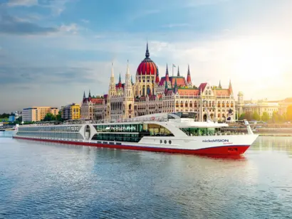 Kreuzfahrtschiff vor Budapest mit Parlament im Sonnenlicht und glitzernder Donau.
