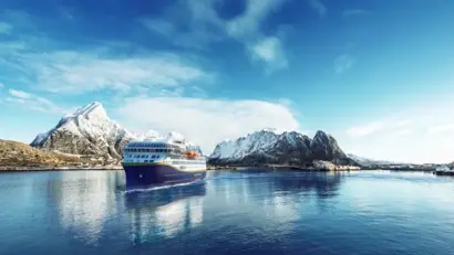 Ein Schiff fährt durch einen tiefen Fjord, umgeben von steilen, beschneiten Berghängen.
