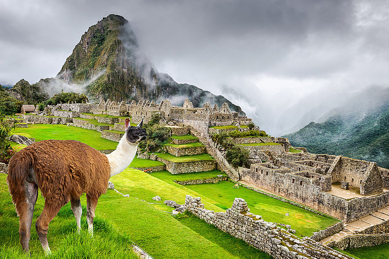 Machu Picchu mit grünen Terrassen, Berggipfeln und dramatischen Wolken.