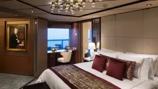 Elegante Schiffssuite mit Doppelbett, Sitzecke, Gemälde und Meerblick durchs Fenster.
