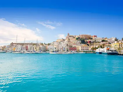 Küstenstadt mit bunten Häusern am Hafen und türkisblauem Meer im Vordergrund.