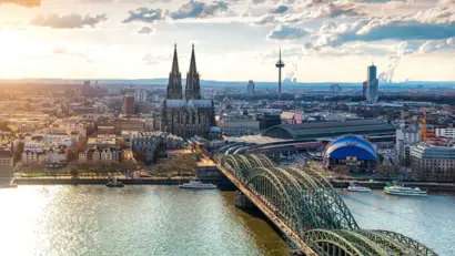 Weitläufiges Stadtpanorama von Köln im Abendlicht mit Fluss, Skyline und Lichtmeer.
