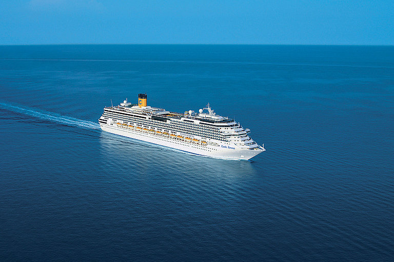 Weißes Kreuzfahrtschiff fährt über ruhiges Meer mit weitem Horizont und blauem Himmel.
