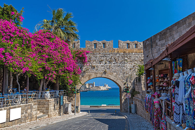 Steingasse mit altem Torbogen, blühender Bougainvillea und historischen Mauern. 