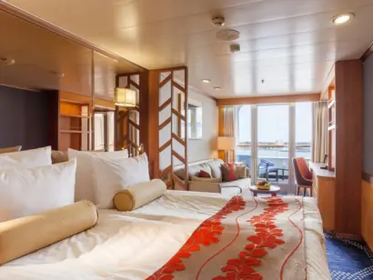 Blick auf helle Schiffskabine auf einem Kreuzfahrtschiff mit rot-beigen Akzenten und Terrasse.