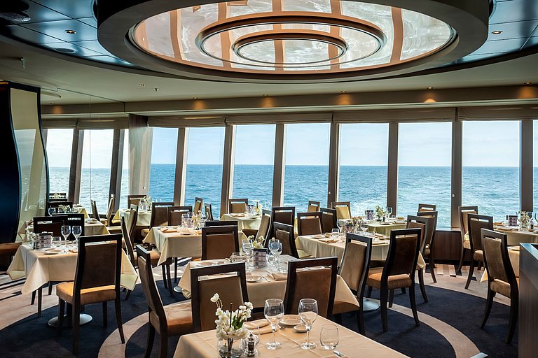 Helles Schiffsrestaurant mit Stühlen, Tischen und schönem Blick auf das dunkelblaue Meer.