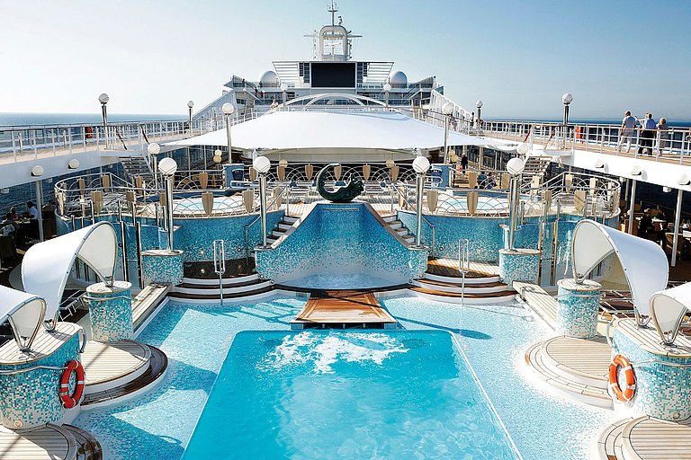 Pooldeck eines Kreuzfahrtschiffs mit Sonnenliegen, Pool, Reling und mehreren Gästen.