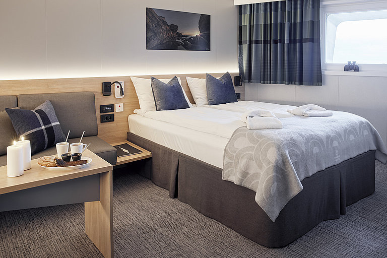 Das Bild zeigt eine Innenkabine mit Doppelbett, kleiner Couch und schönem Teppichboden.