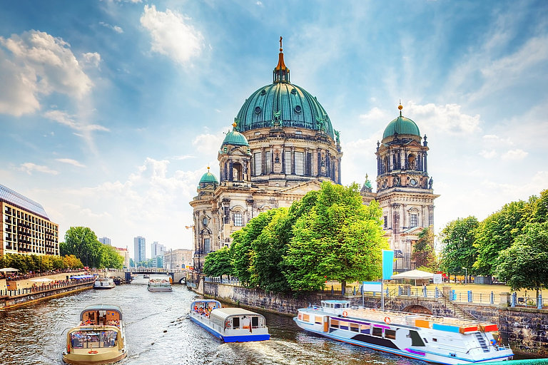 Berliner Dom an der Spree mit Booten und belebter Straße unter Blauem Himmel