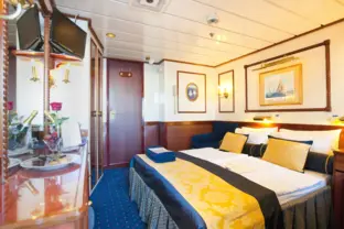 Elegante Kreuzfahrtkabine mit Doppeltbett, Sofa und maritimer Einrichtung an Bord.