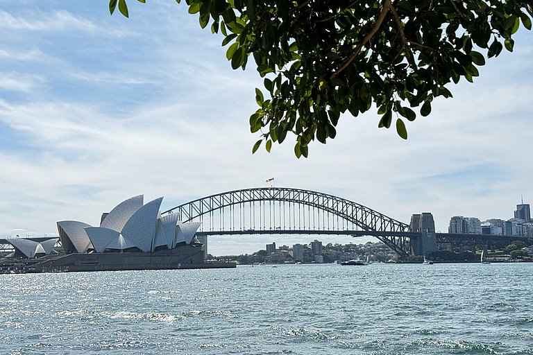Blick auf Sydney Harbour Bridge und Opernhaus über dem Wasser unter hellem Himmel.
