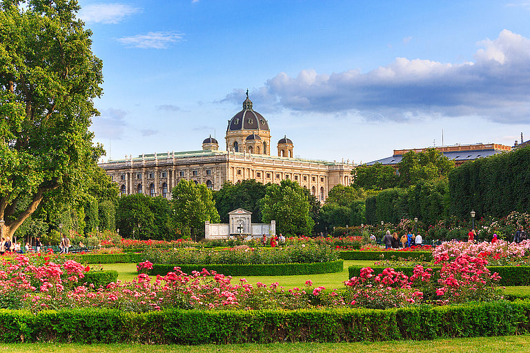 Blühender Garten mit Blick auf historische Stadt und Kuppel unter blauem Himmel.