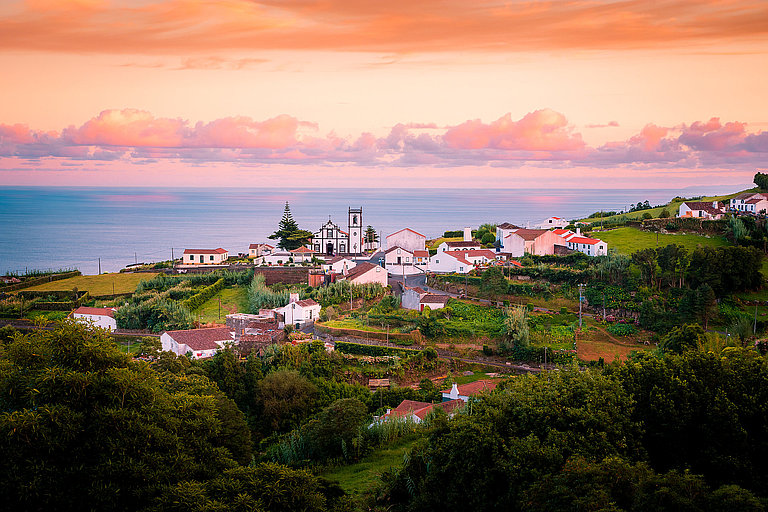 Panoramablick über grüne Hügel und das Meer bei Sonnenuntergang auf São Miguel, Azoren.