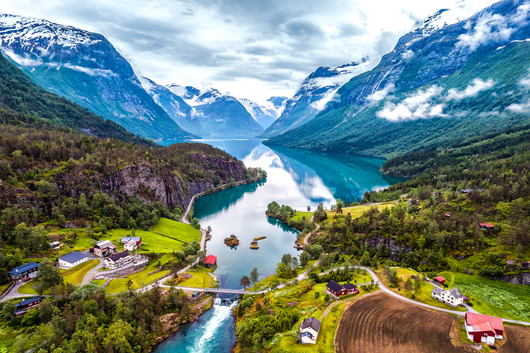 Panoramablick auf Fjorddorf zwischen grünen Tälern und schneebedeckten Bergen.