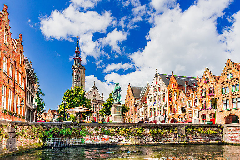 Bruges, Belgium Historische Altstadt mit Kanal, bunten Fassaden und Kirsche unter blauem Himmel.