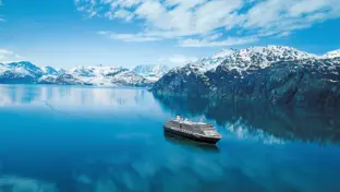 Kreuzfahrtschiff auf türkisblauem Wasser vor schneebedeckten Bergen und Himmel.
