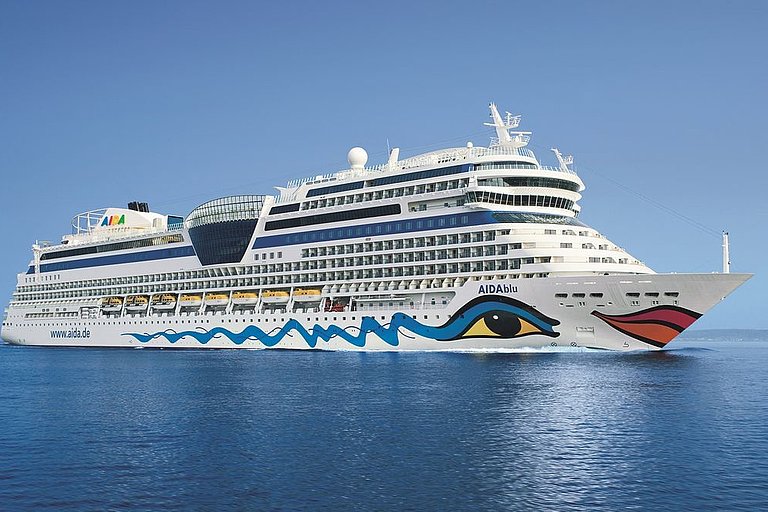 Aida Kreuzfahrtschiff fährt mit Bug- und Heckwelle bei klarem Himmel über das tiefblaue Meerwasser.