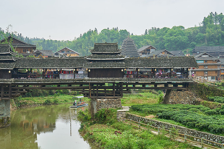 Traditionelle Holzbrücke in Sanjiang über Fluss mit umliegenden Häusern in China