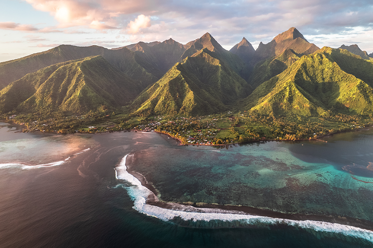 Luftaufnahme einer tropischen Insel mit grünen Bergen, Küste und türkisblauem Meer.