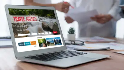 Laptop mit Reiseportal auf einem Tisch, während ein Team im Hintergrund berät.