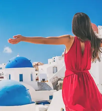 Frau mit rotem Kleid genießt den Blick über weiße Häuser und blaue Kuppeln Santorins.