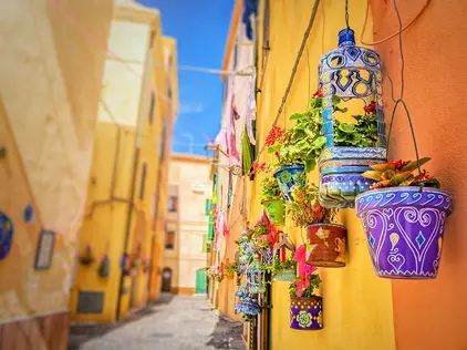 Alghero Street Art Bunte Altstadtgasse auf Sardinien mit Blumentöpfen und warmen Hausfassaden.
