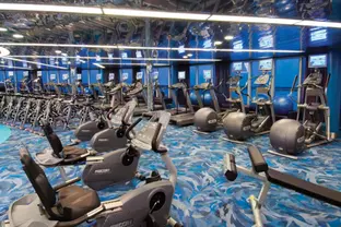 Blick in einen Fitnessraum mit Laufbändern, großen Fenstern und anderen Fitnessgeräten.