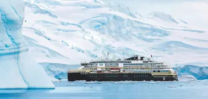 Ein Kreuzfahrtschiff fährt über das türkisblaue Wasser neben Eisschollen vor einem Eisberg.
