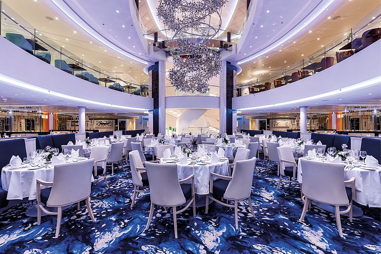 Eleganter Speisesaal an Bord mit gedeckten Tischen und glitzerndem Dekor.