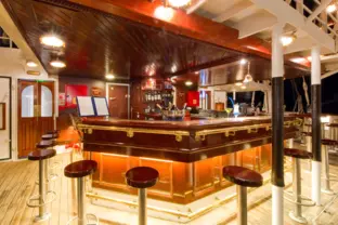 Moderne Bar mit Sitzhockern auf einem Kreuzfahrtschiff mit heller Beleuchtung.