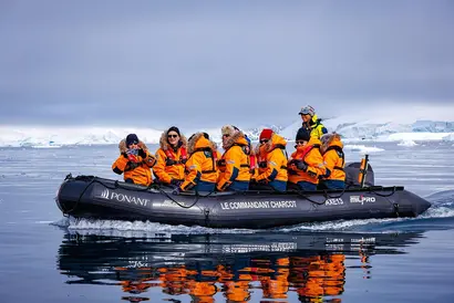 Expeditionsboot mit Passagieren in orangenen Jacken auf ruhigem Wasser zwischen Eis.