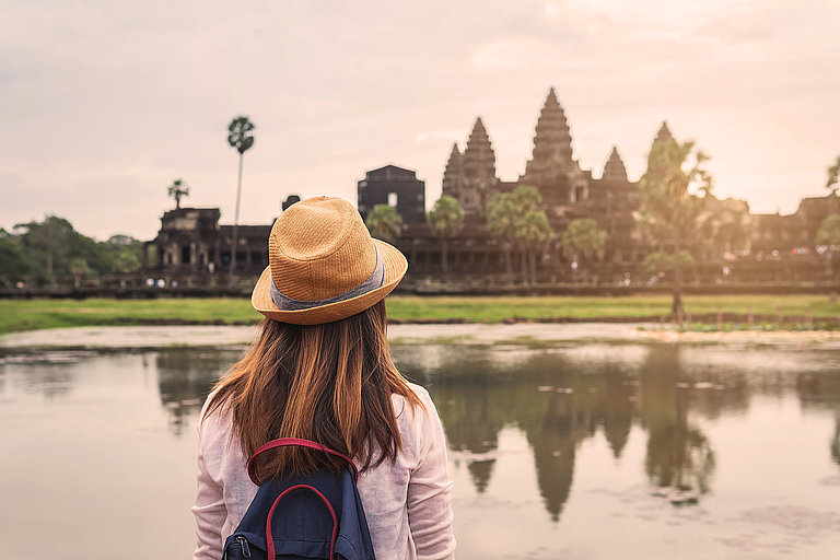 Frau mit Hut blickt über den See auf den Tempel Angkor Wat im Morgenlicht.