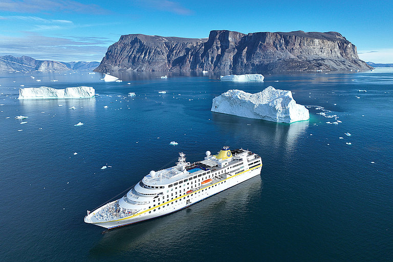 Blick auf ein Kreuzfahrtschiff im Meerwasser zwischen Eisschollen und Inseln.