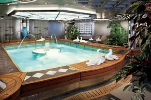 Whirlpoolanlage im Spa an Bord mit Handtuchschwänen, Liegen und tropischer Dekoration.