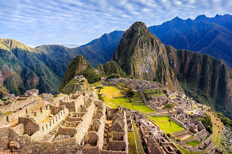 Machu Picchu mit Terrassen, Ruinen und grünen Andengipfeln im Hintergrund.