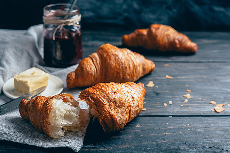 Frische Croissants mit Marmelade und Butter auf dunklem Tisch angerichtet.