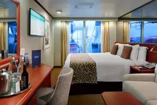 Helle Schiffskabine mit Doppelbett, Sofa, Schreibtisch, Fernseher und Balkonblick aufs Meer.