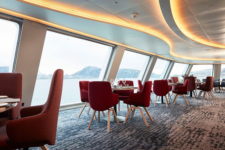 Modernes Restaurant mit roten Stühlen und großen Fenstern auf dem Kreuzfahrtschiff.