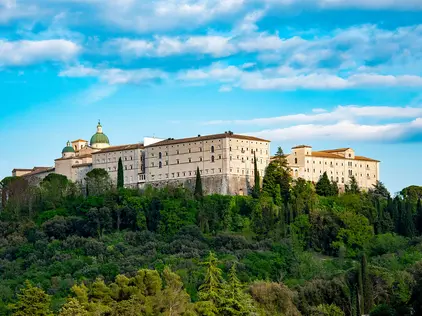 Kloster auf grünen Hügel vor blauem Himmel und mediterraner Landschaft.