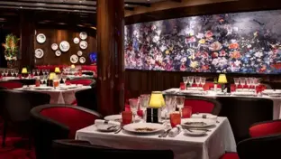 Elegantes Restaurant an Bord mit roten Sitzbänken, gedeckten Tischen und Tellern an der Wand.