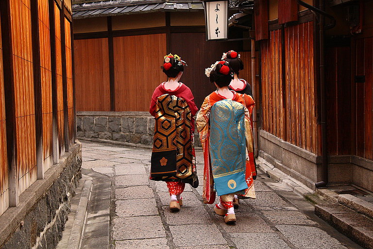 Zwei Frauen in traditionellen Kimonos gehen durch eine schmale historische Gasse.