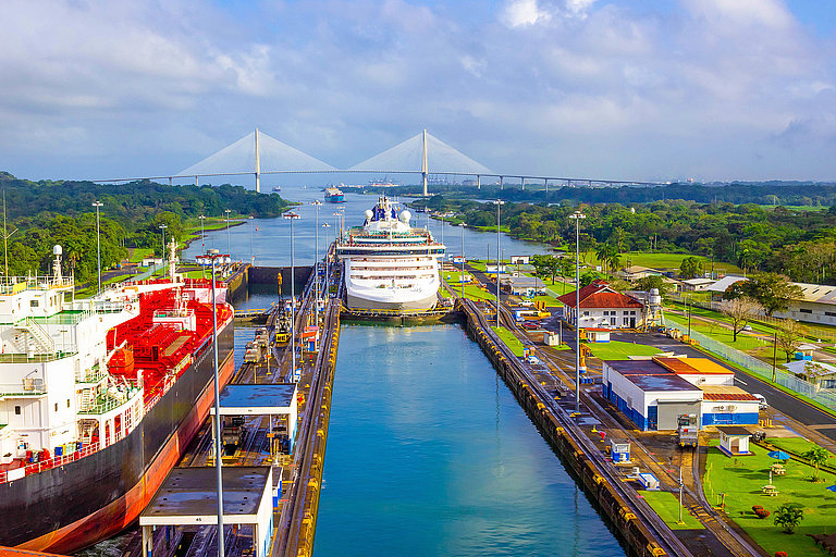 Panamakanal mit Schiff, Schleusen und grüner Landschaft vor moderner Skyline.