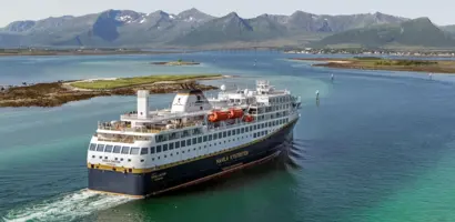 Ein malerisches Dorf mit bunten Häusern und Schiff liegt am Ufer eines ruhigen Fjords.