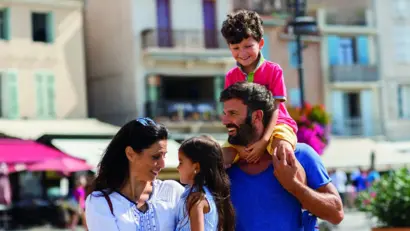 Familie mit bunter Kleidung steht vor einem Hotel und lächelt in die Kamera.