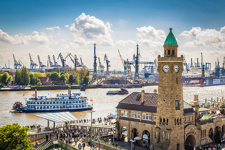 Hafen mit vielen Booten und Menschen vor historischem Turm unter blauem Himmel.