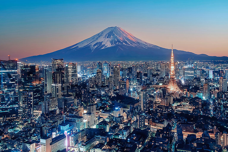 Blick auf Stadt bei Nacht mit Lichtern und schneebedecktem Berg Fuji im Hintergrund.