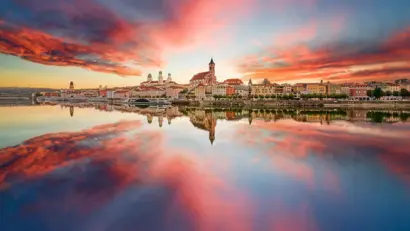Stadtpanorama bei Sonnenuntergang mit farbigem Himmel und Spiegelung im Wasser.