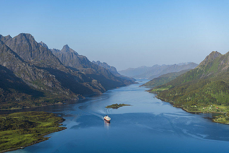 Bergig, grüne Landschaft umgibt einen breiten Fluss mit Kreuzfahrtschiff im Wasser.