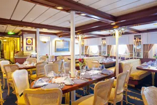 Modernes Restaurant auf einem Kreuzfahrtschiff, mit ovalen Tischen und Sesseln.
