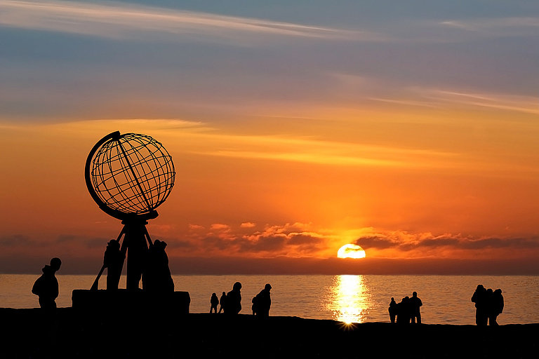 Silhouetten am Nordkap-Globus vor leuchtendem Sonnenuntergang über dem Meer.